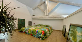 Photo d'une chambre dans les étages du bâtiment, la charpente bois repeinte en blanc participe à l'originalité du lieu.