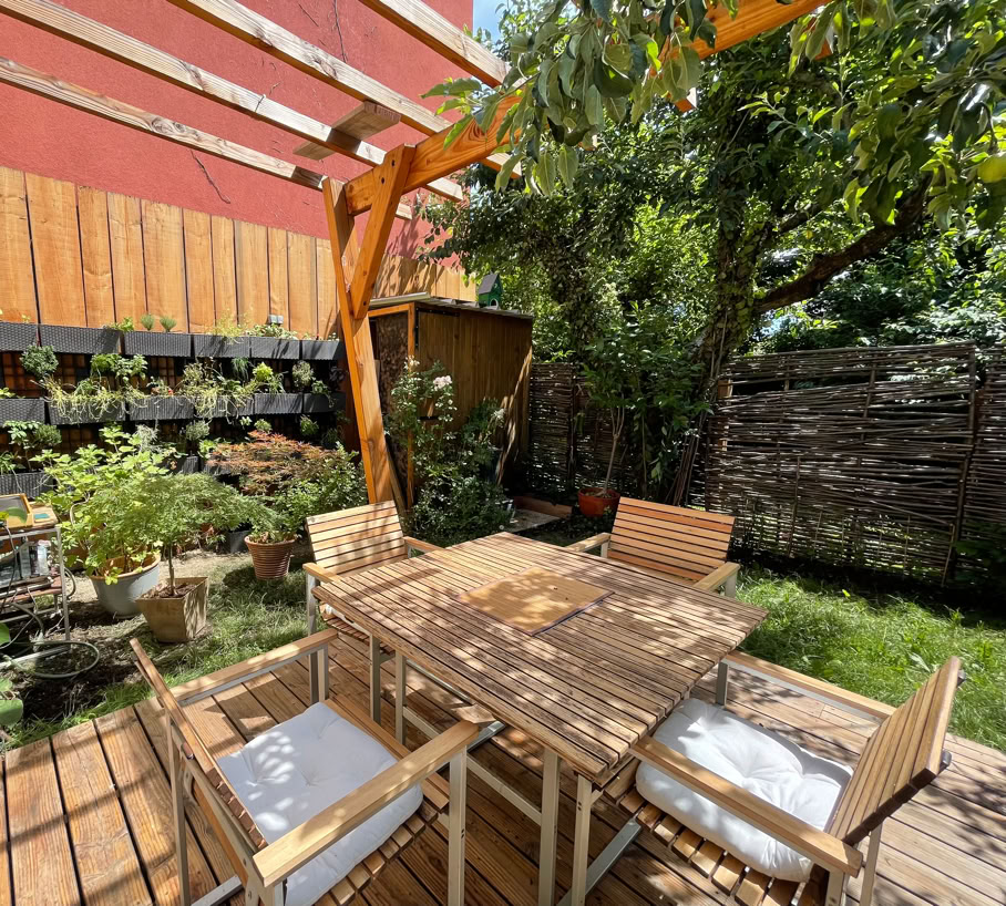 Outdoor wooden terrace with pergola and vegetation.