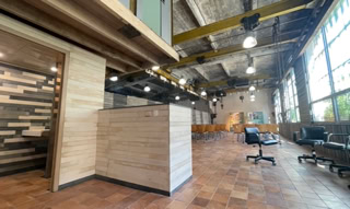 Drittort der grunböx in Wien. Es ist ein großer Saal mit Fliesen, die an die Backsteinfassade erinnern, und in dem die gelben Balken, die bei früheren industriellen Aktivitäten verwendet wurden, in die Einrichtung integriert sind.