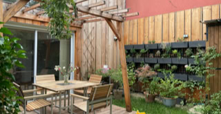 Espace extérieur avec une terrasse bois avec pergolas et beaucoup de végétation.